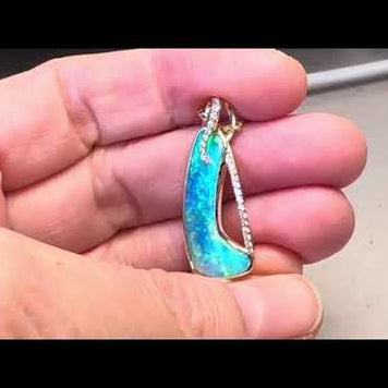 Opal vedhænget har en ægte solid Australsk krystal opal som er indfattet i 14 karat guld. Opalen er 3,42 ct, og har 23 brilliant diamant 0,15 ct. W/SI.